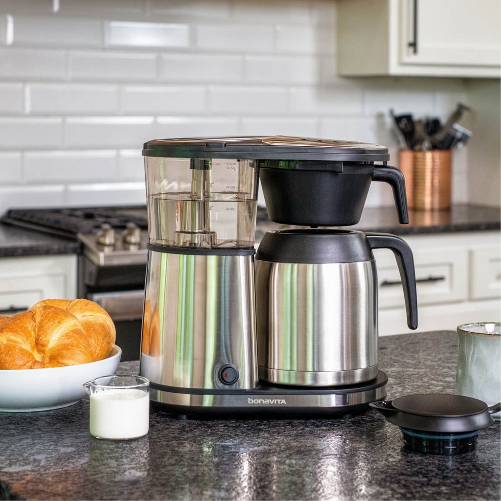 A Bonavita brewer on a walnut kitchen counter at dawn beside ceramic mugs and a bag of fresh coffee beans